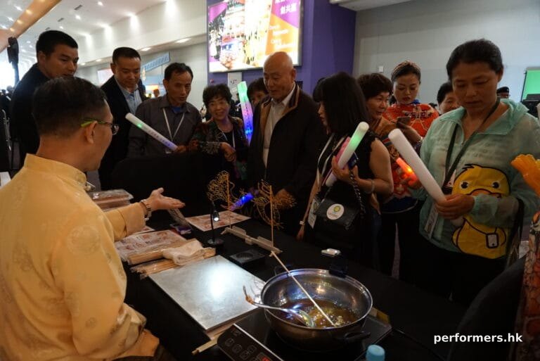 sifu in traditonal costume working at an event doing Sugar painting (糖画), chinese arts and crafts in hong kong
